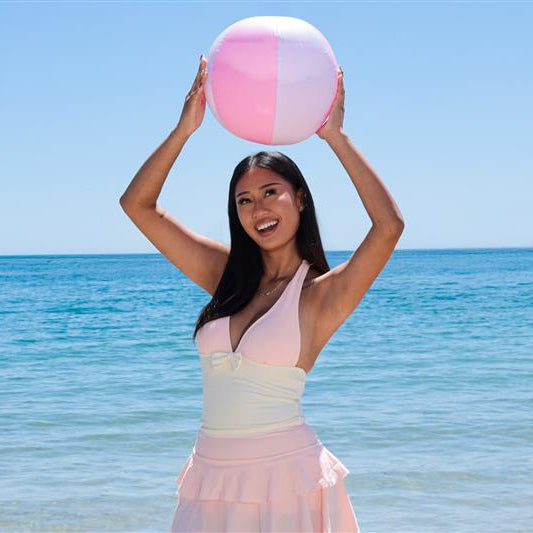 Woman holding a pink and white beach ball on a sunny day at the beach.