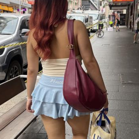 Woman walking on a city street with a maroon handbag and light blue skirt.